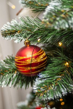 Bir Noel ağacına asılı kırmızı ve altın bir süs. Süs, altın çizgili bir toptur.