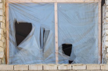 Üzerinde delik olan bir pencere ve bir parça plastik. Plastik yırtılmış ve delik büyük.