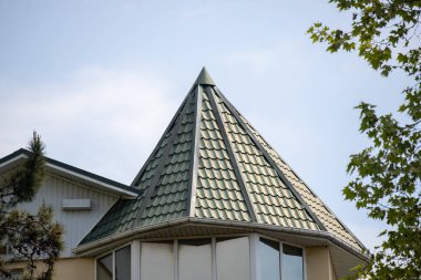 Sivri uçlu yeşil bir çatı. Çatı penceresi olan bir binanın üzerinde. Çatı eğimli ve üçgen şeklinde.