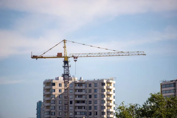 A crane is lifting a large object in front of a tall building. The crane is yellow and is in the air