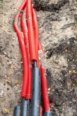 Yerde kırmızı bir boru var. Boru toprakla çevrili ve siyah bir kapağı var.