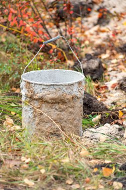 Toprağın içinde sapı olan bir kova var. Kova kirli ve üzerinde bir sürü kir var.
