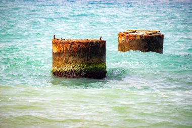 Okyanusta iki eski beton sütun yüzüyor. Su sakin ve gökyüzü berrak.