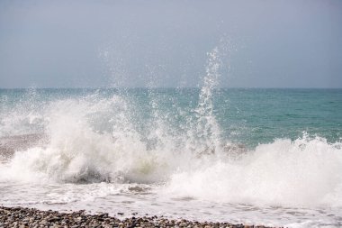 Okyanus dalgalı ve dalgalar kıyıya çarpıyor. Su beyaz ve gökyüzü mavi.