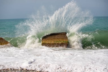 Okyanusta büyük bir kaya var ve su etrafını süzüyor. Sahne sakin ve huzurlu, dalgalar yavaşça kıyıya vuruyor.