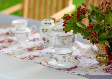 Çiçekli masa taşıyıcısı ve çay seti olan bir masa. Çay takımında çaydanlık, fincan ve çay tabakları var.