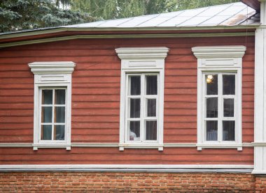 Üç pencereli kırmızı tuğlalı bir bina. Pencereler beyaz ve ahşap çerçeveli. Binanın kırsal bir havası var.