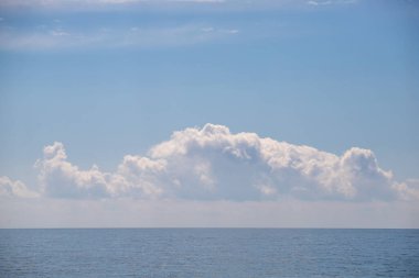 A large cloud is floating over the ocean. The sky is clear and blue, and the water is calm. The scene is peaceful and serene, with the cloud providing a sense of depth