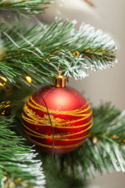 Bir Noel ağacına asılı kırmızı ve altın bir süs. Süs, altın çizgili bir toptur.