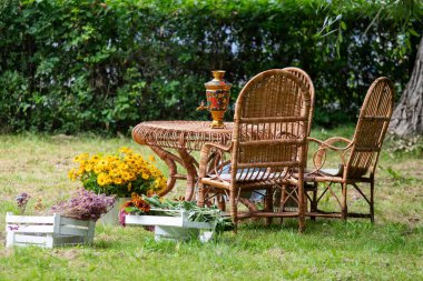 Arka bahçeye bir ahşap masa ve iki sandalye konur. Masada vazo ve çiçekler vardır.