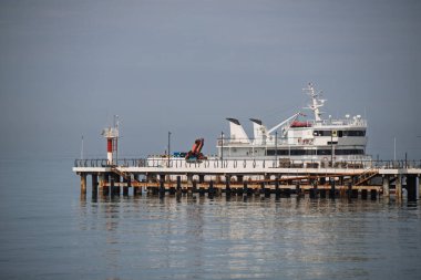 Büyük beyaz bir gemi rıhtıma yanaştı. Su sakin ve gökyüzü kapalı.