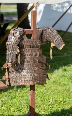 Çimenli bir tarladaki ahşap bir stantta bir zırh sergileniyor. Zırh eski ve paslı, ona bir tarih ve aşınma hissi veriyor. Sahne bir nostalji hissi uyandırıyor.