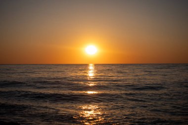 Güneş okyanusun üzerinde batıyor, suyun üzerine sıcak bir parıltı saçıyor. Gökyüzü turuncu ve pembe renklerin bir karışımıdır. Huzurlu ve huzurlu bir atmosfer yaratır. Su sakin ve durgun.