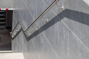 A metal railing on a gray wall. The railing is curved and has a silver color. The wall is also gray and has a tile pattern