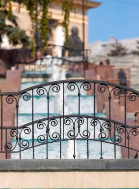 Arka planda şelale olan dövmeli demir bir çit. Çit süslenmiş ve şelale metalin çok güzel bir kontrastı.