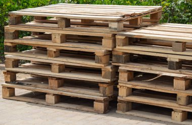 Birkaç tanesi çürümüş bir yığın ahşap palet. Paletler üst üste yığılmış ve çakıl taşı yüzeyindeler.