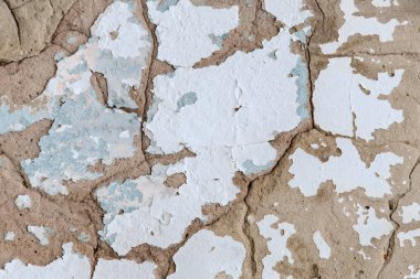 The wall is covered in peeling paint and has a rough texture. The colors are mostly white and blue, with some brown and gray accents. Scene is somewhat bleak and worn