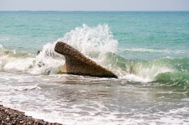 Okyanusta büyük bir kaya var ve su ona çarpıyor. Sahne huzurlu ve sakin, dalgaların sesi ve kayanın yarattığı rahatlatıcı atmosferle.