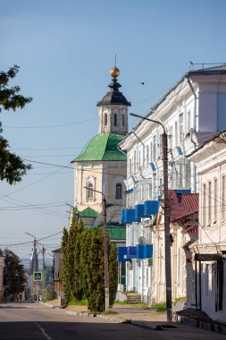 Arka planda yüksek bir bina ve bir kilise olan bir cadde. Sokak ağaçlarla kaplı ve direğin üzerinde mavi bir tente var.