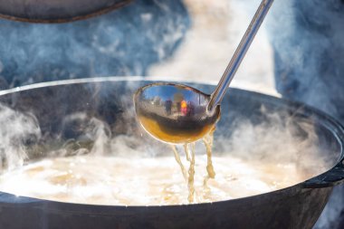 A large pot of soup is being ladled into a bowl. The steam from the soup is rising and the spoon is being used to scoop it out. The scene is warm and inviting