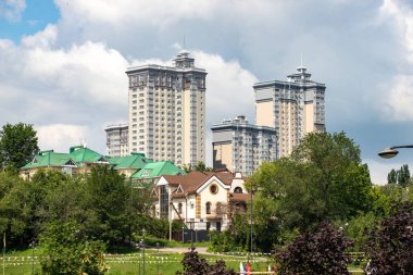 Önünde yüksek binalar ve park olan bir şehir silueti. Gökyüzü bulutlu ve binalar çoğunlukla beyaz.
