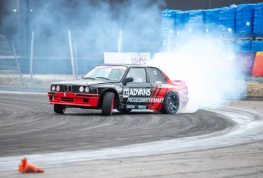 Arkadan duman çıkan bir araba pistte gidiyor. Arabanın sponsoru Adidas ve virajı dönüyor.