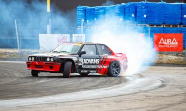 Arkadan duman çıkan bir araba pistte gidiyor. Aracın sponsoru Adams ve yarış pistinde.