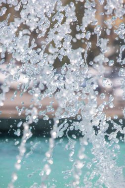 A stream of water is falling from a fountain, creating a beautiful and calming atmosphere. The water droplets are clear and sparkly, reflecting the sunlight and creating a sense of tranquility