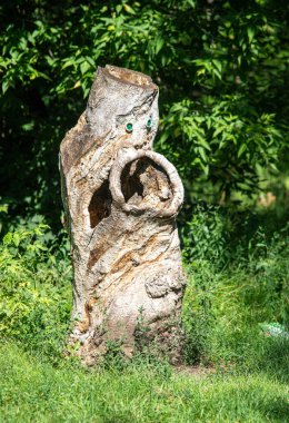 Ağaç gövdesine oyulmuş bir yüz. Kütük çimenler ve ağaçlarla çevrili. Bu kütüğün tüyler ürpertici bir görüntüsü var. Hayalet ya da ruh izlenimi veriyor.