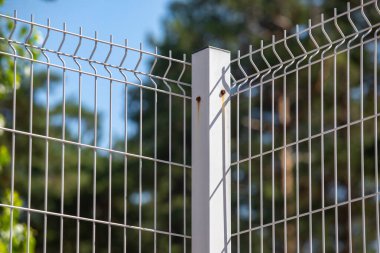 A white metal fence with a brown post. The fence is made of wire and has a lot of holes