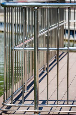 A metal railing with a red sign on it. The railing is on a dock near a body of water