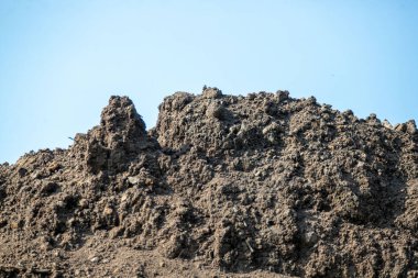 Arka planda mavi gökyüzü olan kayalık bir yamaç. Tepe toprak ve kayalarla kaplı ve gökyüzü berrak ve parlak.