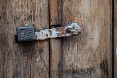 Paslı bir kilit ahşap bir kapıya bağlıdır. Kilit 5 numarasıyla etiketlenmiş. Kapı eski ve yıpranmış, ahşap bir çerçevesi ve ahşap bir kapısı var. Kilit paslanmış ve adam bakımsız.