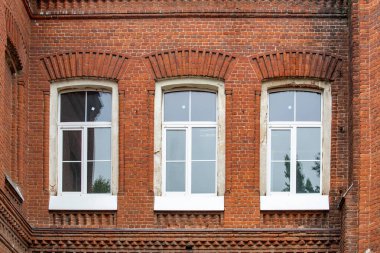 Beyaz çerçeveli tuğla bir binanın üç penceresi. Pencereler hafif eğimli ve bina eski.