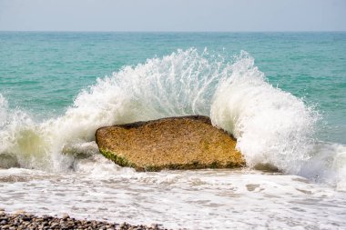 Okyanusta büyük bir kaya var ve su üzerine dökülüyor. Güç ve güç kavramı, dalgalar kayanın üzerine kuvvetle vururken. Sahne dinamik ve enerji dolu.