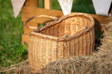 Bir sepet saman yığınının üzerinde duruyor. Sepet hasırdan yapılmış ve sapı var. Samanlar kahverengi ve sepetin etrafına saçılmış. Sahne kırsal ve rahat bir hava veriyor.