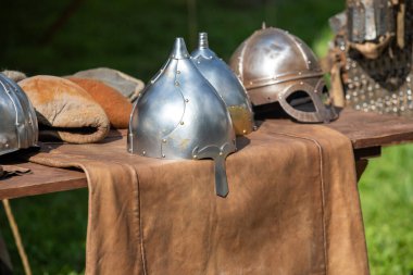 Ahşap bir masada bir çift kask ve deri eldiven sergilenir. Kasklar gümüş, eldivenler kahverengi. Sahne macera ve heyecan hissi veriyor.