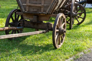 Çimenli bir arazide ahşap bir araba tekerleği duruyor. Tekerlek eski ve yıpranmış ve yeşil çimlerle çevrili. Nostalji ve basitlik kavramı