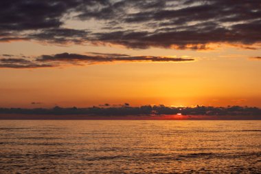 Güneş okyanusun üzerinde batarken gökyüzü güzel turuncu bir renktir. Su sakin ve huzurlu, sakin bir atmosfer yaratıyor.