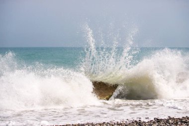 Okyanus dalgalı ve dalgalar kayalara çarpıyor. Su beyaz ve gökyüzü mavi.