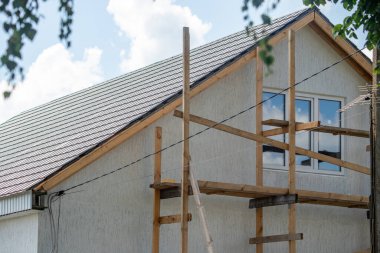 İnşaat halindeki bir evin yan tarafında iskele var. Ev beyaz ve eğimli bir çatısı var.