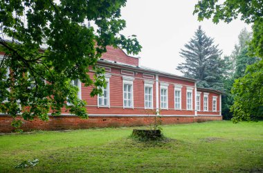 Beyaz süslemeli büyük kırmızı tuğla bir bina çimenli bir arazide oturur. Binanın önünde bir sürü pencere ve büyük bir ağaç var.