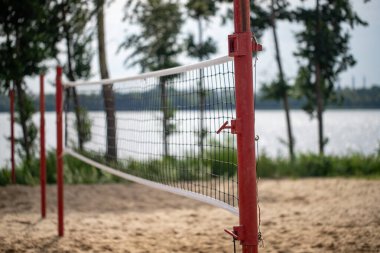 Kırmızı bir voleybol ağı kumlu bir sahilde, bir su kütlesinin yanında. Ağ, kullanılmayan bir şekilde kurulmuş.