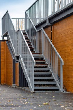 Arkasında ahşap bir duvar ve parmaklık olan bir merdiven. Korkuluklar metalden, merdivenler de ahşaptan yapılmıştır.