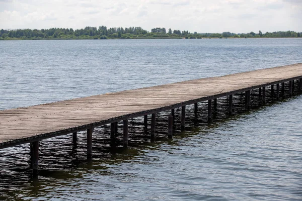 Tahta bir köprü bir su kütlesini kapsar. Su sakin ve gökyüzü bulutlu. Köprü eski ve yıpranmış, ama hala sağlam.
