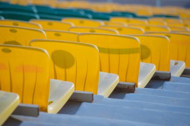 Bir sıra sarı sandalye tribüne dizilmiş. Sandalyeler aynı yöne bakıyor.