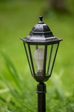 İçinde ampul olan siyah bir lamba direği. Ampul beyaz bir LED. Lamba direği çimenli bir alanda.