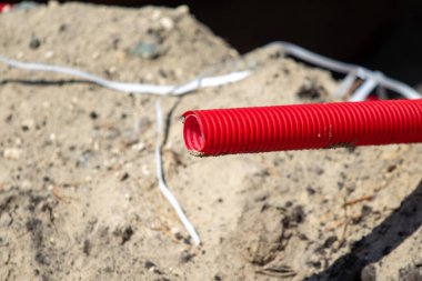 Kumlu bir alanda yerden kırmızı bir boru çıkıyor. Boru kablolar ve diğer döküntülerle çevrili. Bölgede inşaat veya onarım işi kavramı