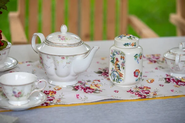 Çiçekli bir masa koşucusuyla birlikte bir çay seti bir masada sergilenir. Masa çay partisi için hazırlandı, fincanlar, çay tabakları ve çaydanlık. Masa koşucusu biraz renk katar