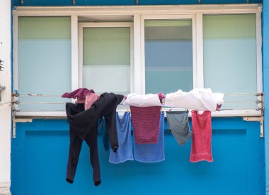 A row of clothes hanging on a clothesline outside. The clothes are of different colors and sizes. The clothesline is attached to a wall